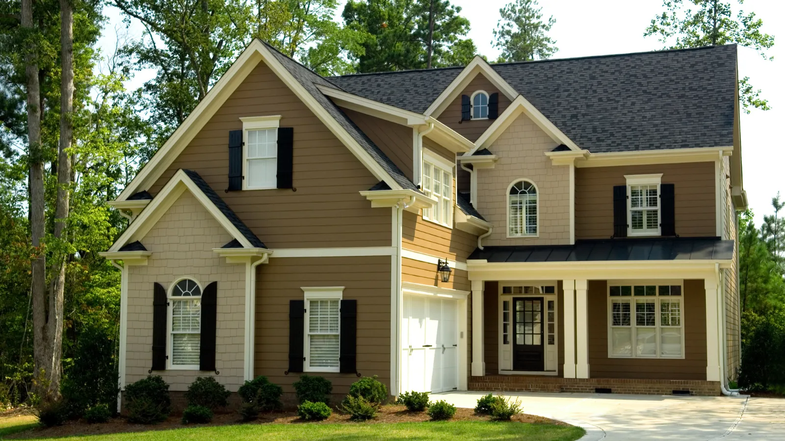 Dark shingle roof and white garage door on a brown two-story house